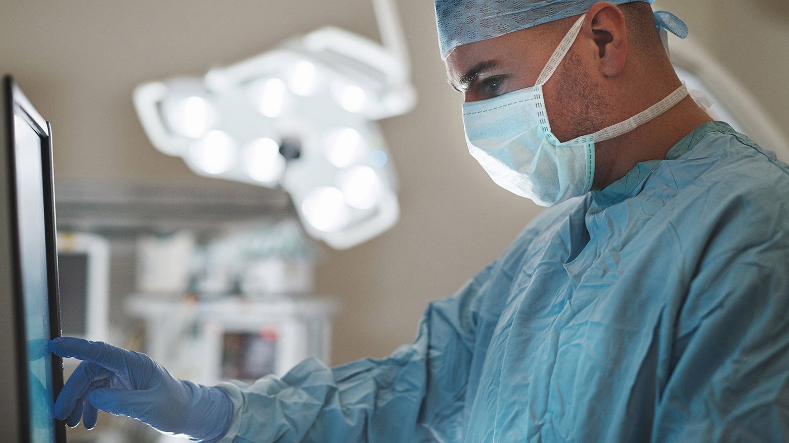 A male doctor wears a medical mask and looks at a computer screen