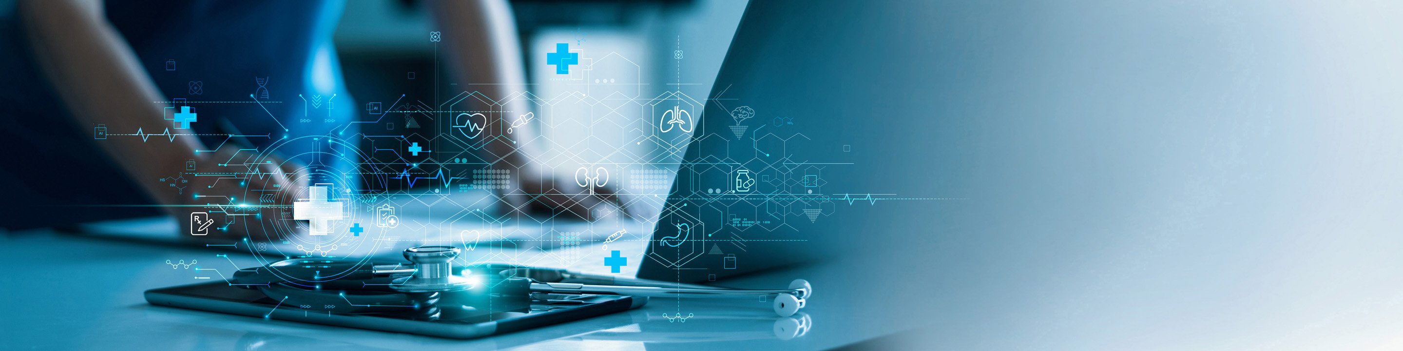 A laptop, tablet and stethoscope are seen in front of a medical professional. 